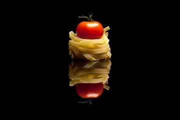 Nest pasta with red tomato black reflective background