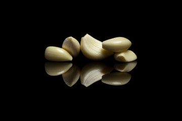 Five peeled garlic on black reflective background