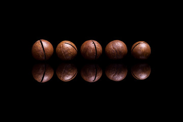 Five macadamia nuts on black reflective background