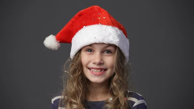 Close up smiling little girl in a red santa's cap against gray background