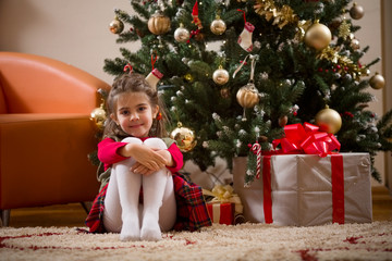Happy child girl with Christmas gifts sitting near a Christmas tree