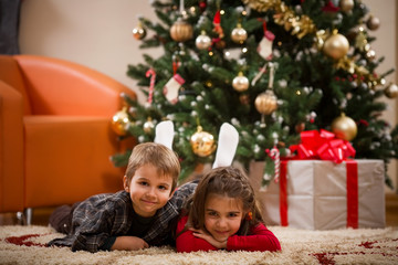 Fototapeta na wymiar Happy kids laying on the floor in front of the christmas tree and smiling