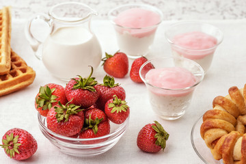 On the table in a glass Cup strawberries. Strawberries scattered on the table. In the glass cups the yogurt. In the saucer lies a cookie. Studio light. Lifestyle