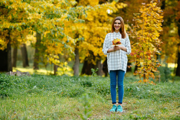  Brunette girl walking in the autumn park with leaves in her hands.