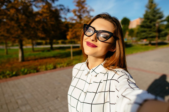 Pretty woman is drawing in the autumn sun while taking a selfie with her smartphone.