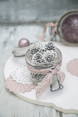 Weisse Laerchenzapfen in einem Weckglas dekoriert auf einem weissen Holzbrett mit rosa und lila farbenen Weihnachtskugeln.