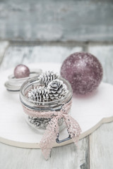 Weisse Laerchenzapfen in einem Weckglas dekoriert auf einem weissen Holzbrett mit rosa und lila farbenen Weihnachtskugeln.
