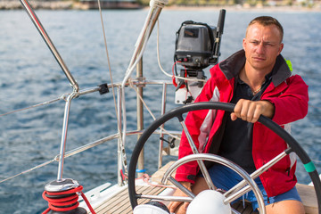 Naklejka premium Skipper at the helm controls of a sailing yacht.