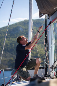Yachtsman pulls the rope on the mast, on his sailing yaht boat on the sea.