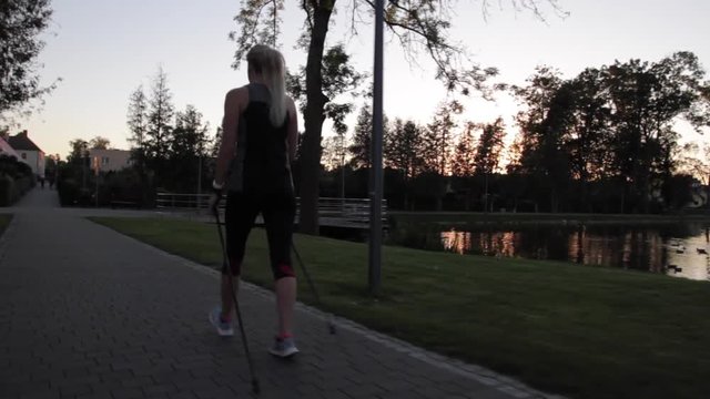 Dziewczyna uprawiająca nordic walking w parku o zachodzie słońca.