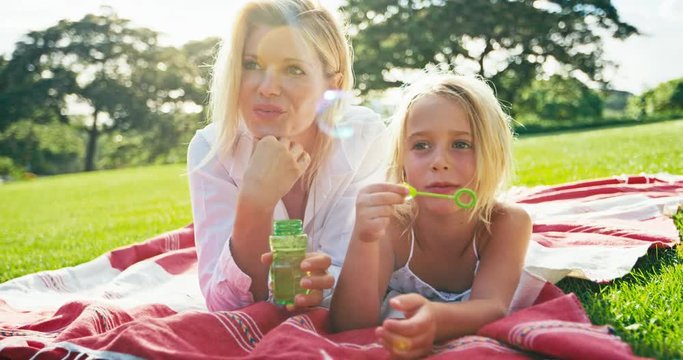 Mother and daughter relaxing together blowing bubbles in the park