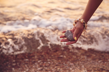 Woman holding stone near sea at sunset