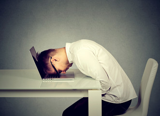 Desperate employee stressed young man resting head on laptop keyboard
