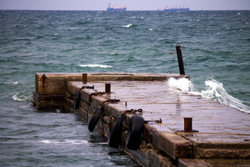 Old pier with rustly bollards and fenders with two vessels on the background