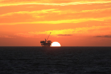 Beach off-shore oil rig platform at sunset