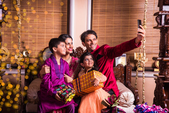 Asian Indian family taking selfie or self photograph at home with gift boxes on diwali festival. Parents and children indoor lifestyle. Indian family celebrating diwali and taking selfie on phone