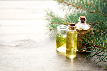 Bottles of coniferous essential oil and branches on wooden background, close up view