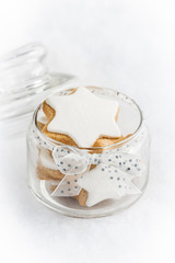 Fototapeta na wymiar Close up of a glass jar full with christmas homemade star cookies over white fluffy background.