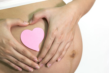Pregnant woman is hands shape heart around pink paper note on be