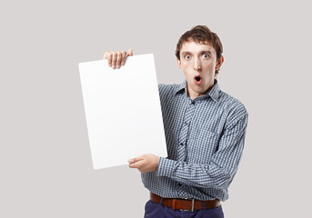 shocked man with a sheet of white paper in hands. guy opened his mouth in surprise. young man holding a blank sheet of white paper for your text. looking at camera. mockup. isolated on grey background