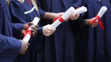 students in bachelor gowns holding diploma scrolls