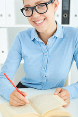 Closeup of a female student at workplace with book holding red pencil studying. Education, self development and perfection concept