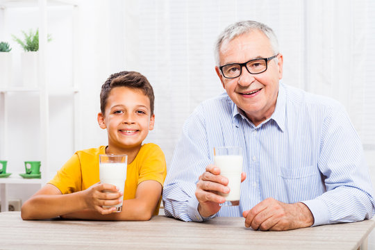 Grandfather and grandson are drinking milk at home. Healthy lifestyle. 