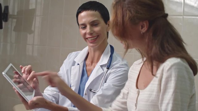 Cheerful female doctor showing woman ultrasound scan picture on tablet and explaining it