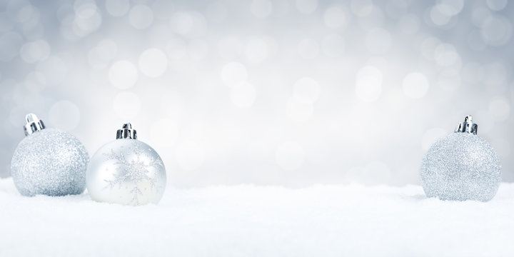 Silver Christmas baubles on snow with a silver background