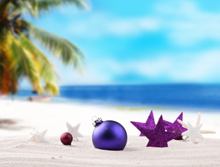 Christmas purple ball, ornament on a beach - concept of a warm weather Christmas