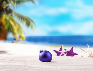 Fototapeta na wymiar Christmas purple ball, ornament on a beach - concept of a warm weather Christmas