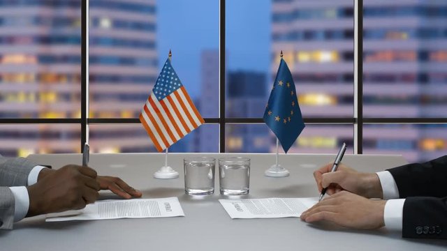 Businessmen in suits sign papers. Flags of EU and USA. New intercontinental alliance. Progress and order.