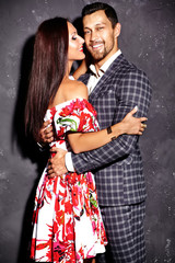 Fashion photo of smiling handsome  elegant man in suit with beautiful sexy woman posing near gray wall