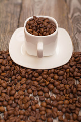 small white cup with coffee beans on wooden background