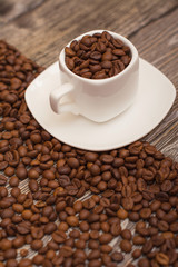 small white cup with coffee beans on wooden background