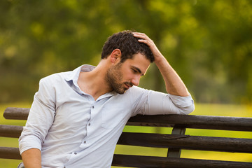 Depressed businessman is sitting at the park and thinking about something.
