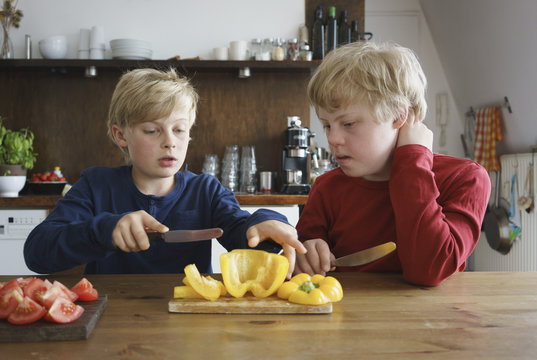 Boy assisting brother to chop bell pepper at table in kitchen