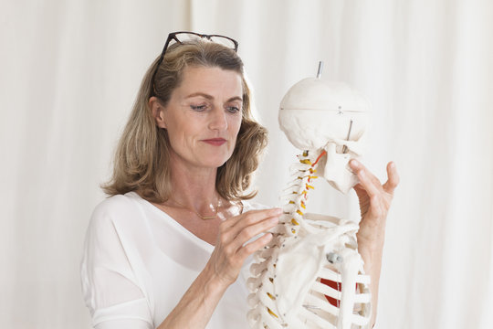 Confident female doctor looking at skeleton while standing in clinic