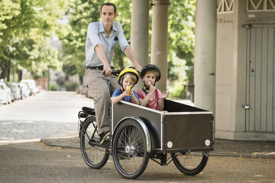 Father with boys riding bicycle with cart on street