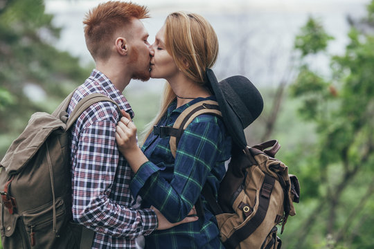Loving couple wearing backpacks kissing while standing at forest