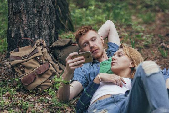 Young couple looking in smart phone while lying by tree at forest
