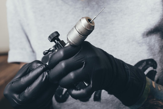 Midsection of tattoo artist wearing gloves holding equipment at art studio