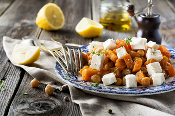 Warm salad of pumpkin, chickpeas and feta cheese on the old wooden background. Selective focus.