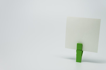 Piece of Memo paper clamped by green wooden clip with white background and selective focus