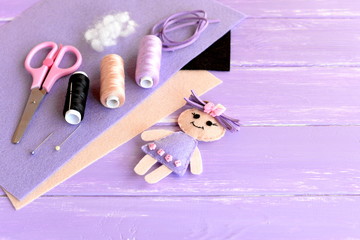 Set for kids activity and creativity. Felt doll, scissors, thread, needles, pins, pliers, suede cord, felt sheets on wooden background with empty space for text. Easy kids diy