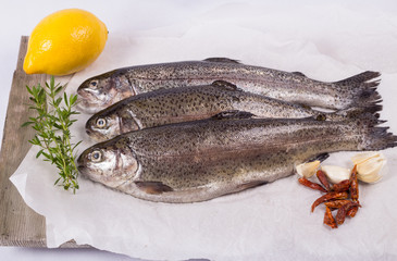 Three raw trouts on paper with thyme and lemon on a rustic wooden table