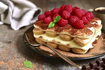 Tiramisu with raspberry on a black plate.