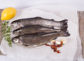 Three raw trouts on paper with thyme and lemon on a rustic wooden table