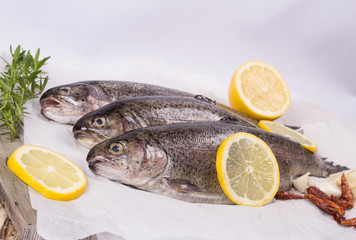 Three raw trouts on paper with thyme and lemon on a rustic wooden table