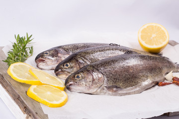 Three raw trouts on paper with thyme and lemon on a rustic wooden table